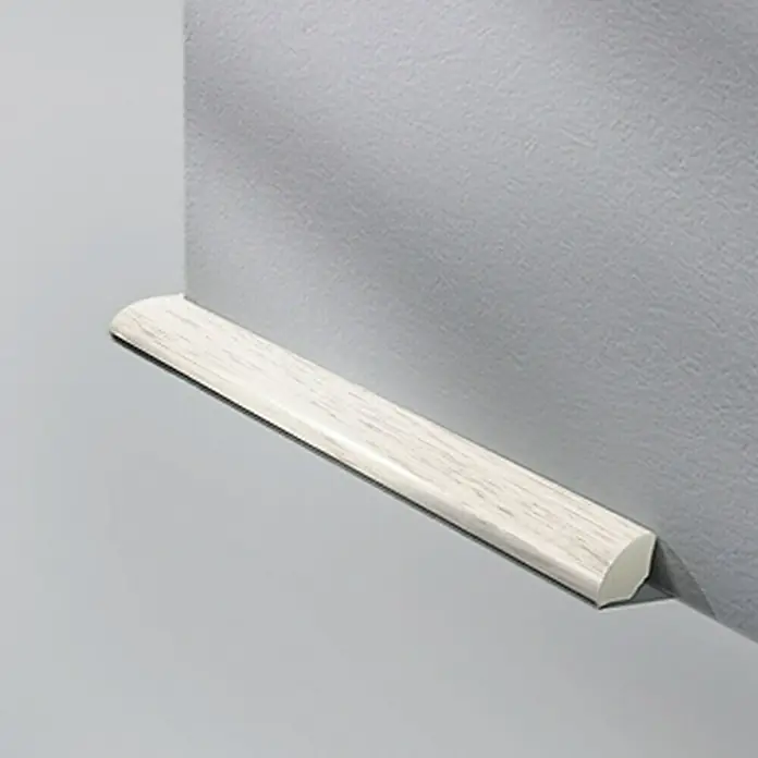 LOGOCLIC Viertelstab Esche Weiß - 250 cm x 14 mm x 14 mm - Eine Nahaufnahme einer weißen Holzfußleiste an einer grauen Wand, die die Maserung und Form des Produkts hervorhebt.