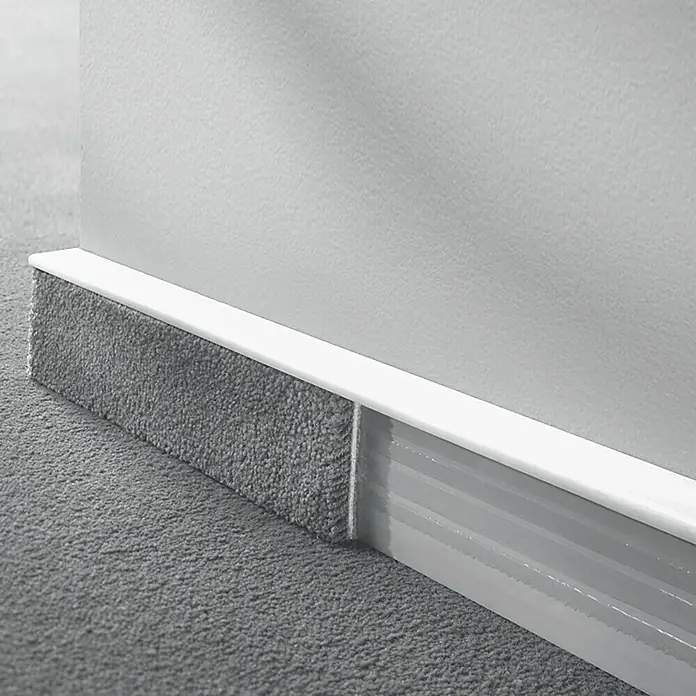 LOGOCLIC Sockelleiste TSL - 250 cm x 16 mm x 55 mm, Weiß - Nahaufnahme einer Fußleistenheizung mit Teppichbesatz und weißer Abdeckung vor einer weißen Wand.