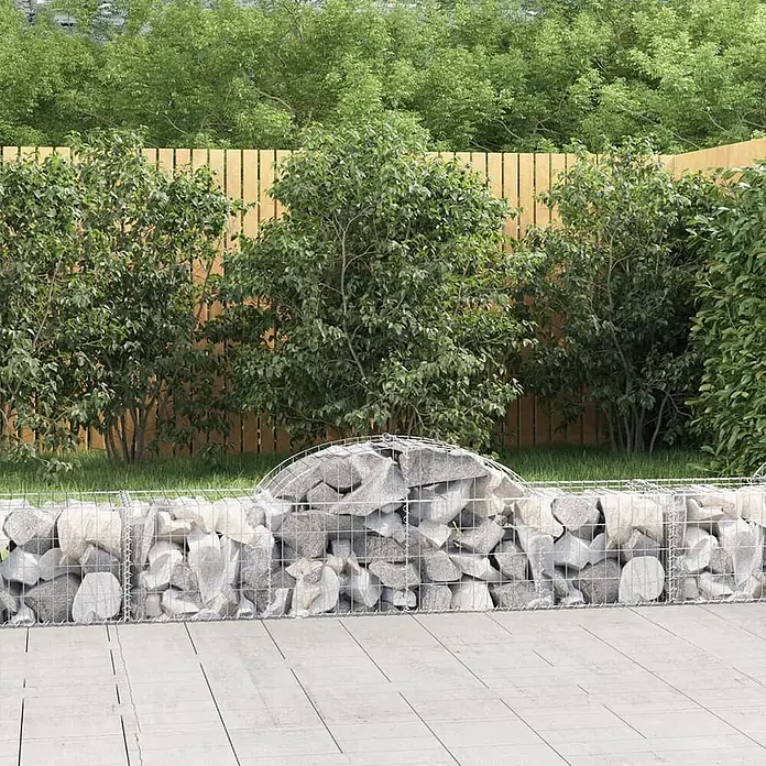 Furnicato Gabione - 60 x 200 x 50 cm, Metall, Maschenbreite: 50 mm, Maschenhöhe: 100 mm - Geschwungene Gabionenwand, gefüllt mit hellgrauen Steinen, als Gartenbank auf einer Terrasse.