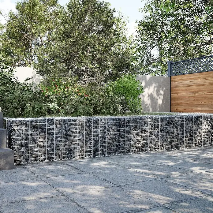 Furnicato Gabione - 300 x 50 x 50 cm, Metall, Maschenbreite: 50 mm, Maschenhöhe: 100 mm - Gabionen-Stützmauer aus Metallgitter mit grauen Steinen, trennt gepflasterten Bereich von Gartenlaub.