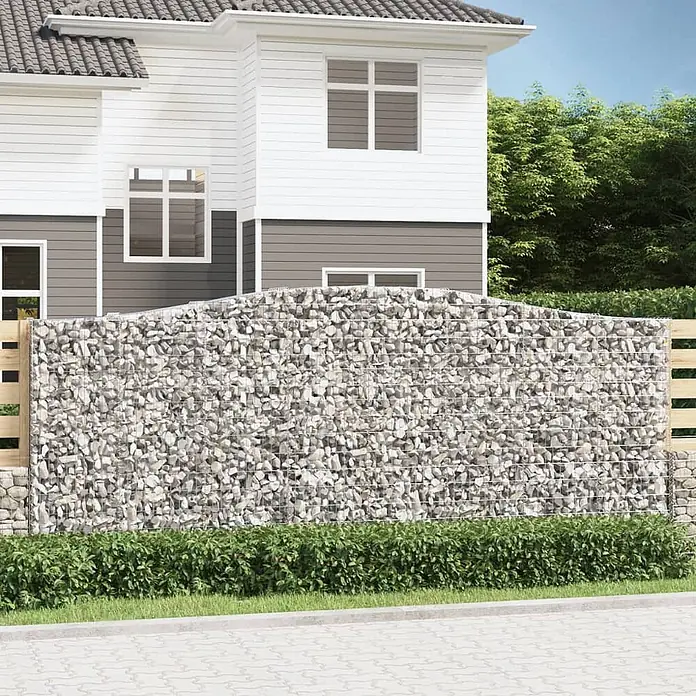 Furnicato Gabione - 180 x 400 x 50 cm, Metall, Maschenbreite: 50 mm, Maschenhöhe: 100 mm - Gabionenzaun mit hellgrauen Steinen und geschwungener Oberkante, dient als Gartengrenze vor einem Haus.