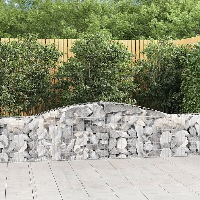 Furnicato Gabione - 30 x 400 x 80 cm, Metall, Maschenbreite: 50 mm, Maschenhöhe: 100 mm - Niedrige Gabionenmauer aus Metallgeflecht mit hellgrauen Steinen, in einem Garten.