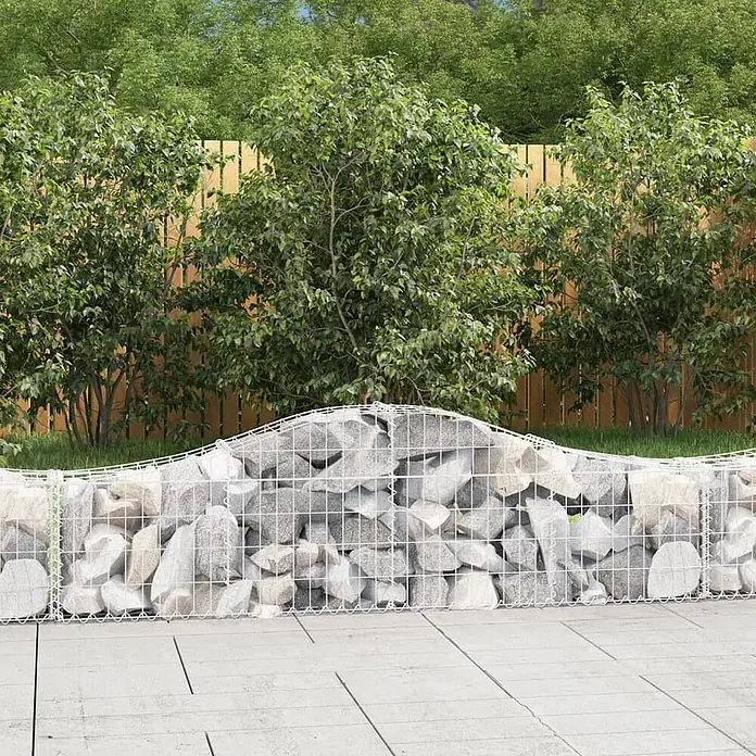 Furnicato Gabione - 30 x 200 x 60 cm, Metall, Maschenbreite: 50 mm, Maschenhöhe: 100 mm - Wellenförmige Gabionenwand mit grauen Steinen in weißem Gitter, grenzt eine Terrasse im Gartenbereich ab.