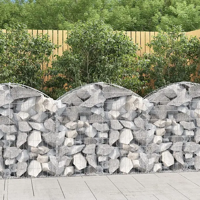 Furnicato Gabione - 100 x 100 x 30 cm, Metall, Maschenbreite: 50 mm, Maschenhöhe: 100 mm - Gabionenwand mit gewelltem Oberteil, gefüllt mit grauen Steinen, in einem Garten vor einem Holzzaun und grünen Büschen.