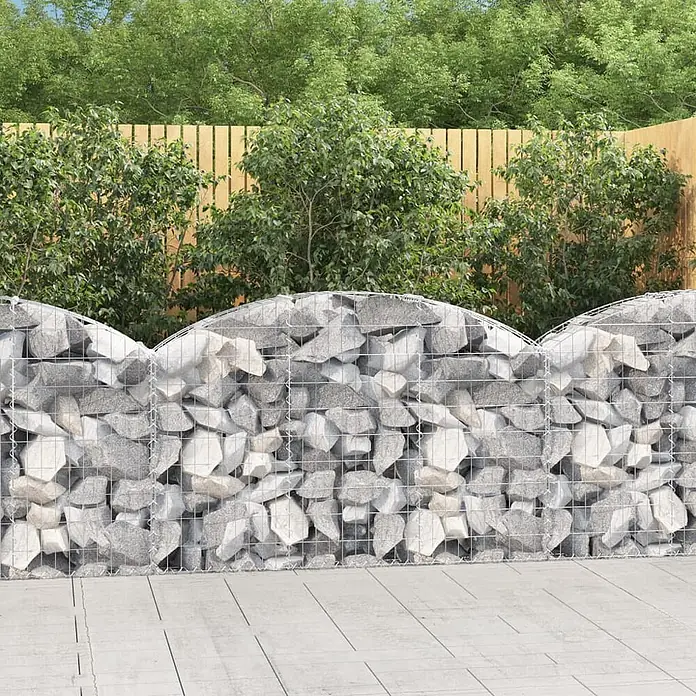 Furnicato Gabione - 30 x 150 x 100 cm, Metall, Maschenbreite: 50 mm, Maschenhöhe: 100 mm - Gabionenwandzaun mit wellenförmiger Oberkante, gefüllt mit grauen und weißen Steinen, der einen Gartenbereich abgrenzt.