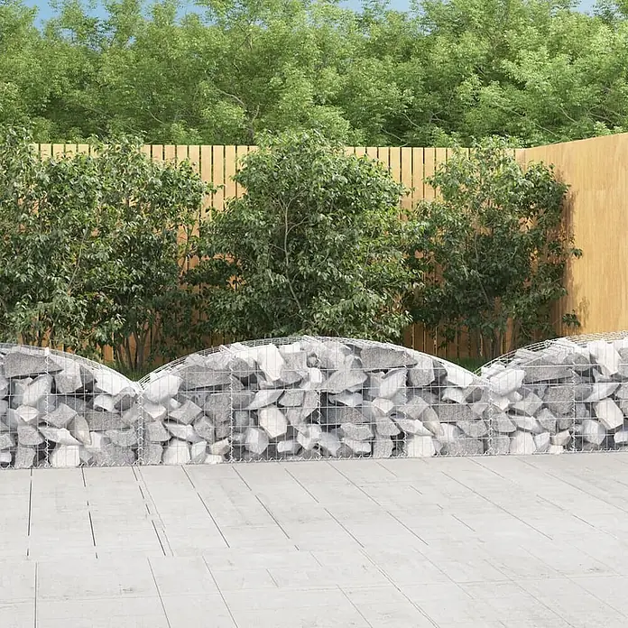 Furnicato Gabione - 60 x 200 x 50 cm, Metall, Maschenbreite: 50 mm, Maschenhöhe: 100 mm - Wellenförmige Gabionenmauern, gefüllt mit grauen Steinen, dienen als dekorativer Gartenteiler auf einer Terrasse.