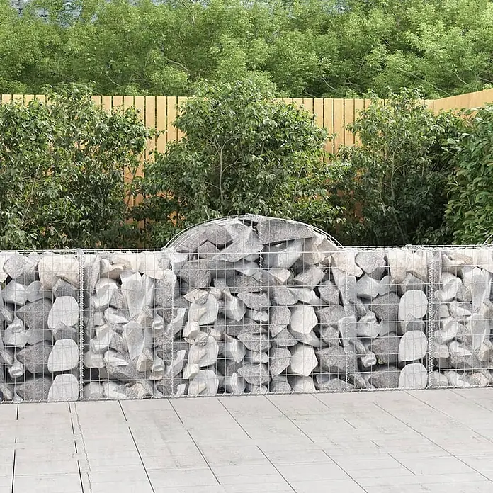 Furnicato Gabione - 50 x 200 x 100 cm, Metall, Maschenbreite: 50 mm, Maschenhöhe: 100 mm - Graue Gabionenwand aus Steinen mit gewölbter Oberseite in einem Garten mit Holzzaun und Grün.