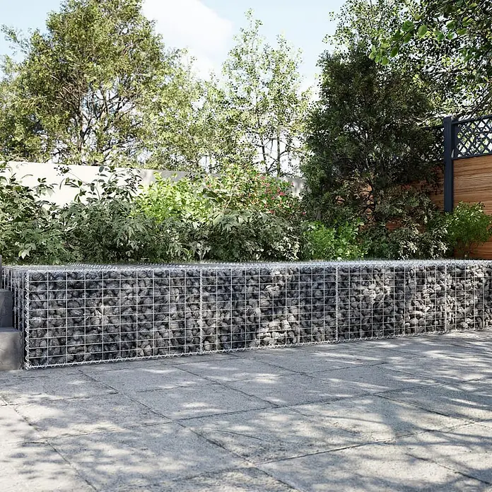 Furnicato Gabione - 300 x 100 x 50 cm, Metall, Maschenbreite: 50 mm, Maschenhöhe: 100 mm - Gabionenwand mit dunklen Steinen, umrahmt von Drahtgeflecht, in einer Gartenumgebung.
