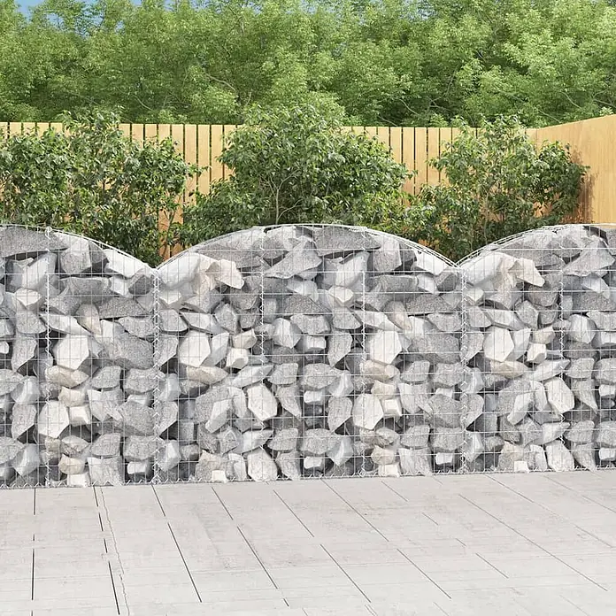 Furnicato Gabione - 30 x 150 x 120 cm, Metall, Maschenbreite: 50 mm, Maschenhöhe: 100 mm - Gabionenwand aus grauen Steinen im Metallgitter mit Wellenform oben, die einen Gartenbereich teilt.