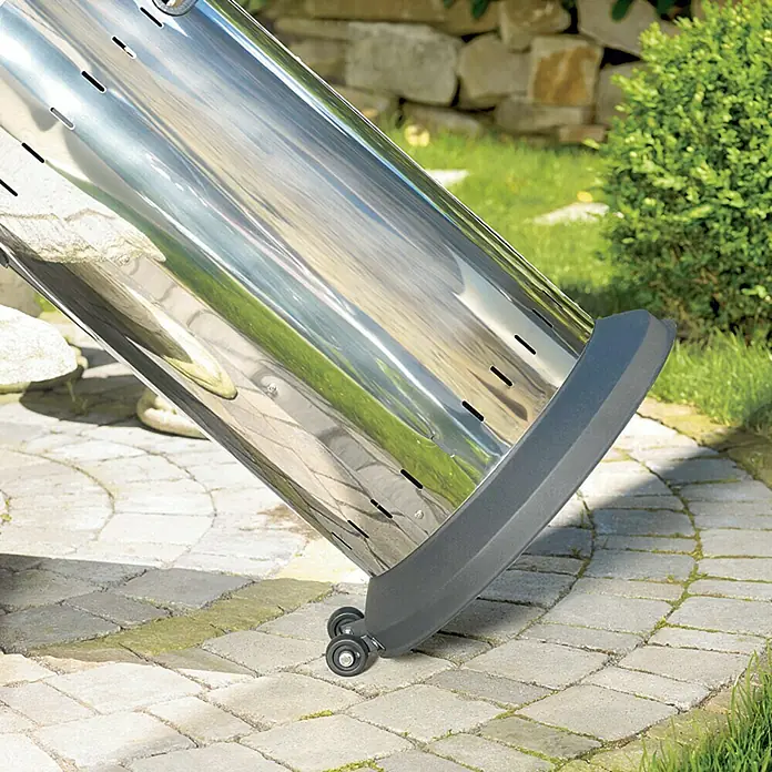 Enders Estufa de exterior Elegance - Potencia calorífica: 3,5 kW - 8 kW, Altura: 218 cm - Primer plano de un calentador de patio de acero inoxidable con ruedas sobre un patio pavimentado, rodeado de vegetación.