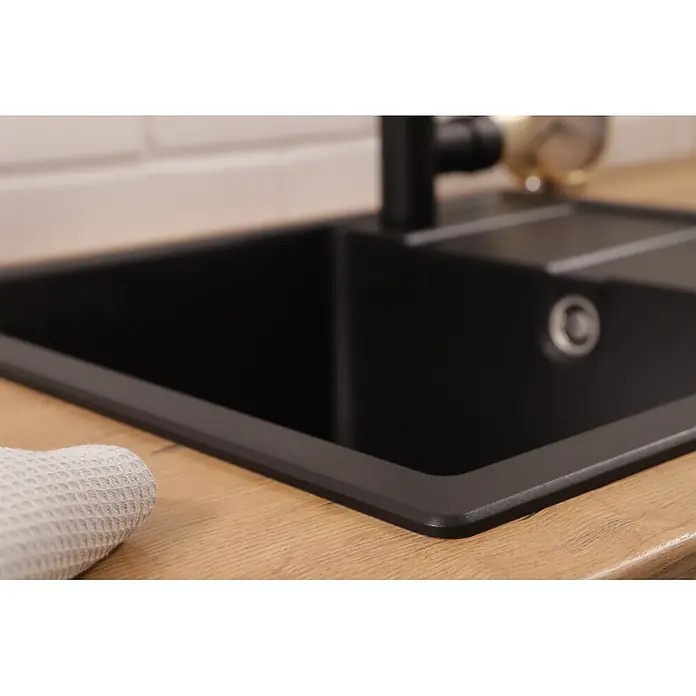 Respekta Einbauspüle Nashville - 58 x 50 cm, Schwarz - Schwarze Granit-Küchenspüle mit schwarzem Wasserhahn in einer Holzarbeitsplatte. Ein weißes Handtuch liegt daneben.