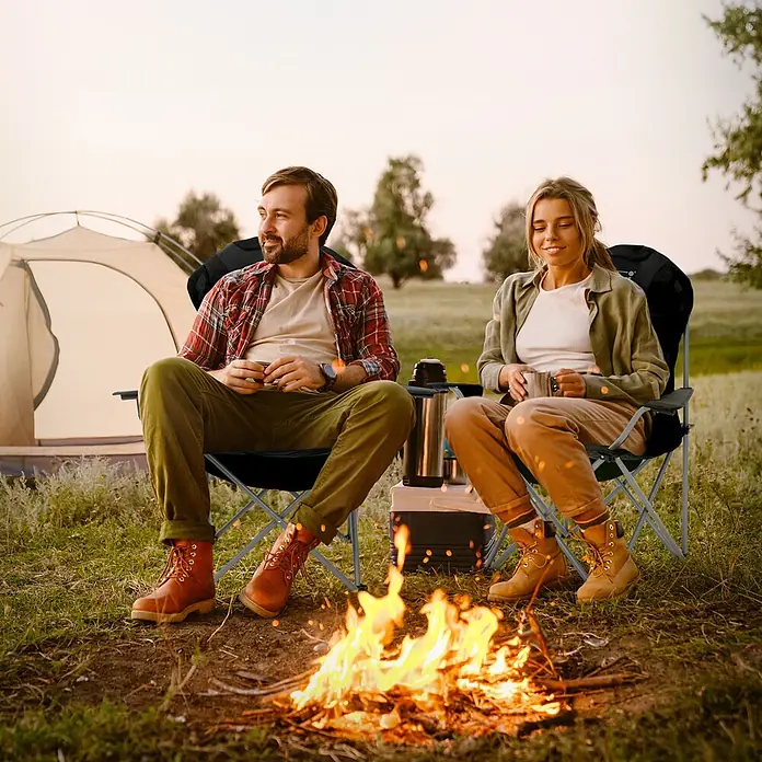 Hauki Campingstuhl 2er Set Klappstühle Schwarz gepolsterte Angelstühle mit hoher Rückenlehne - Stahl, Polyester, Klappbar, Schwarz - Zwei schwarze Klapp-Campingstühle mit Metallrahmen, genutzt von einem Paar am Lagerfeuer.