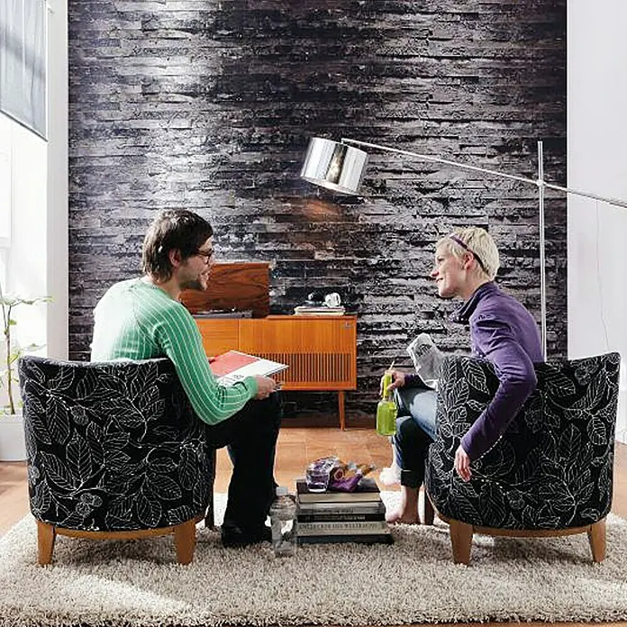 Komar Imagine Edition 3 - Stories Fototapete Birkenrinde - 8 -tlg., B x H: 368 x 254 cm, Papier - Zwei Sessel mit schwarzem Blätterdruckmuster und Holzbeinen auf einem weichen Teppich, ideal für ein gemütliches Wohnzimmer.