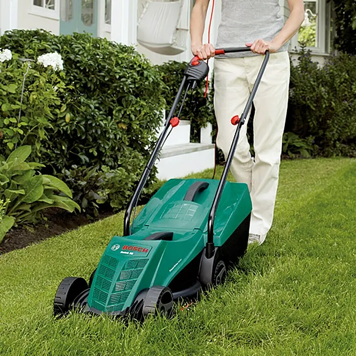 Bosch Elektro-Rasenmäher Rotak 32 - 1.200 W, Schnittbreite: 32 cm - Eine Person benutzt einen grünen Bosch Rasenmäher, um den Rasen vor einem Haus zu mähen.