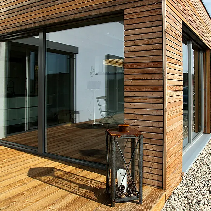 Profilholz Rhombus - 200 x 7 x 2,8 cm, Douglasie - Detailaufnahme eines modernen Hauses mit Holzwand, Fensterfront und einer dekorativen Laterne mit Kerze auf der Holzterrasse.
