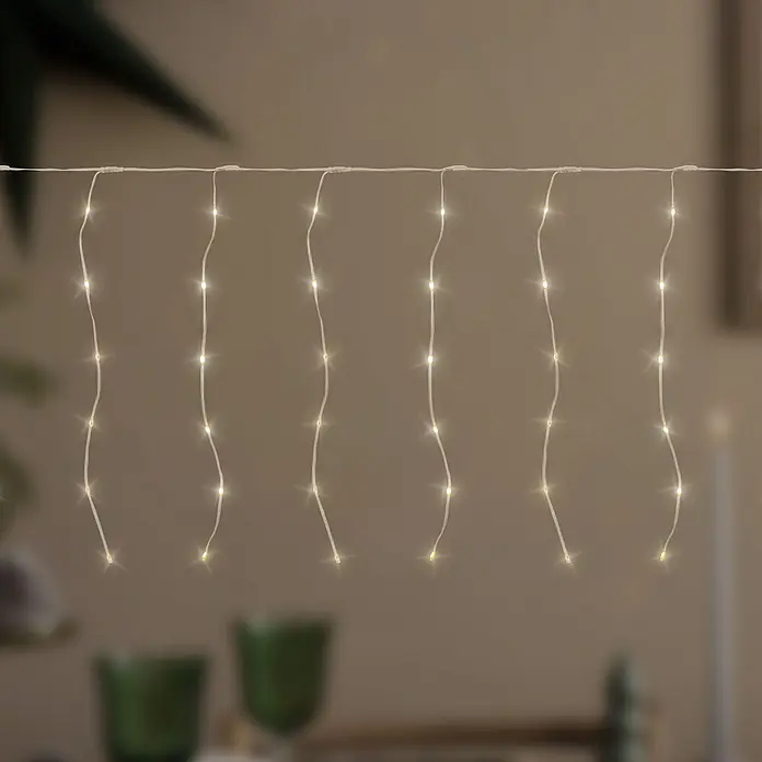 ECD Germany LED-Lichtervorhang 120 LEDs 3m für Innen & Außen IP44 Warmweiß - Innen, Warmweiß, 120 Stk., Netzbetrieben - Warmweiße LED-Lichterkette mit dünnen weißen Drähten, vertikal hängend vor unscharfem Innenhintergrund.