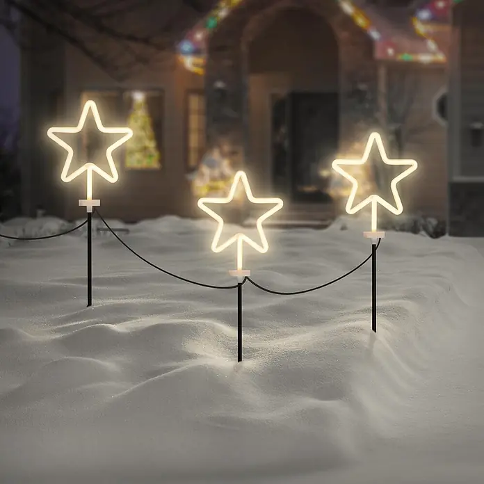 ECD Germany LED-Weihnachtsdekofigur 3er Set Gartenstecker Stern Deko Beleuchtung für Außen Stableuchten - 500 x 1,8 x 58 cm, Weiß, Netzbetrieben, LED - Drei leuchtende sternförmige Wegleuchten mit dunklen Erdspießen und Verbindungskabel beleuchten einen verschneiten Gartenweg vor einem festlichen Haus.