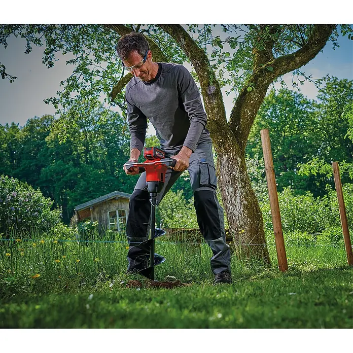 Einhell Professional Akku-Erdbohrer - 18 V, Ohne Akku, Durchmesser: 150 mm - Mann in Arbeitskleidung nutzt roten und schwarzen Akku-Erdbohrer zum Graben eines Lochs im Garten.