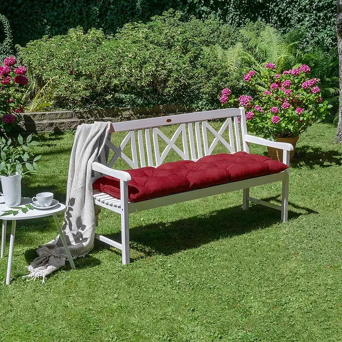 Beautissu Bankauflage Flair BK - Gartenbank, 1 Stk., L x B x H: 100 x 50 x 10 cm, Polyester, Rot - Weiße Gartenbank mit rotem Kissen für Entspannung im Freien, in einem grünen Garten platziert.