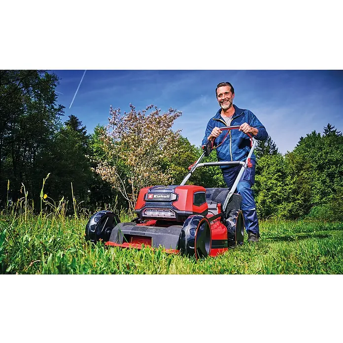 Einhell Professional PXC 18V Akku-Rasenmäher GP-CM 36/47 S HW Li - 36 V, 4 Akkus, 4 Ah, Schnittbreite: 47 cm - Mann lächelt, während er einen rot-schwarzen Einhell Rasenmäher zum Gras schneiden in einer grünen Umgebung benutzt.