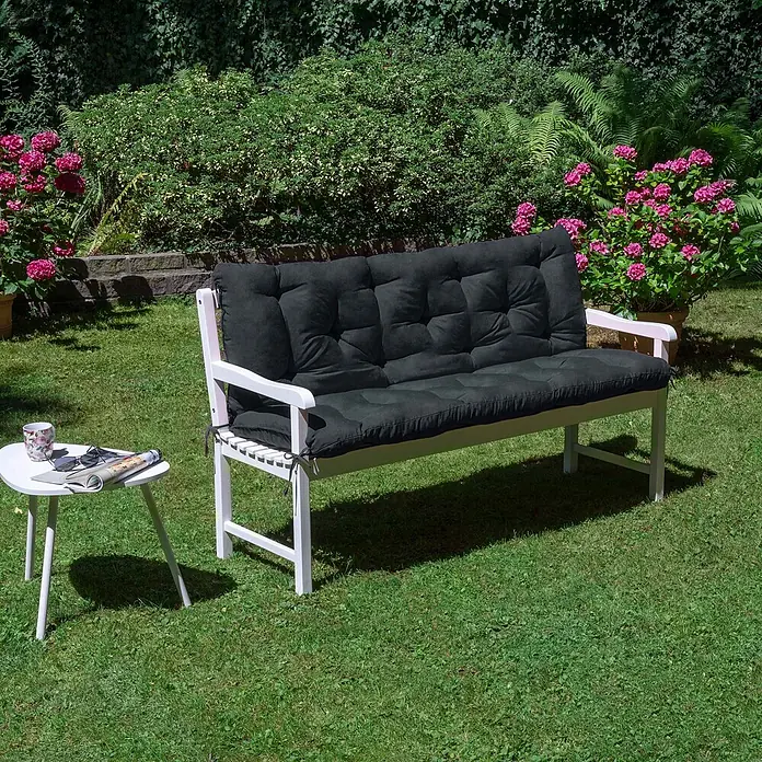 Beautissu Bankauflage Flair BR - Gartenbank, 1 Stk., L x B x H: 180 x 50 x 10 cm, Polyester, Graphitgrau - Weiße Gartenbank mit dunkelgrauen Kissen, draußen aufgestellt mit einem Beistelltisch.