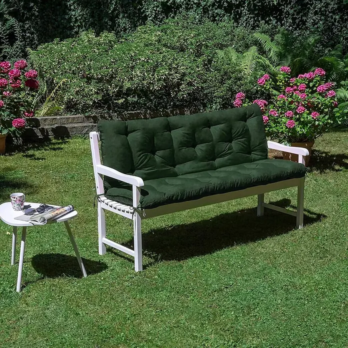 Beautissu Bankauflage Flair BR - Gartenbank, 1 Stk., L x B x H: 100 x 50 x 10 cm, Polyester, Dunkelgrün - Weiße Gartenbank mit dunkelgrünen gesteppten Kissen, in einem sonnigen Garten mit einem kleinen weißen Beistelltisch.