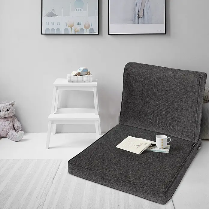 Beautissu Sitzauflage Ilano - Outdoor Lounge, 2 Stk., L x B x H: 60 x 60 x 23 cm, Polyester, Graphitgrau - Dunkelgrauer Bodensessel aus Stoff mit Rückenlehne, mit Buch und Tasse, auf einem hellen Teppich.