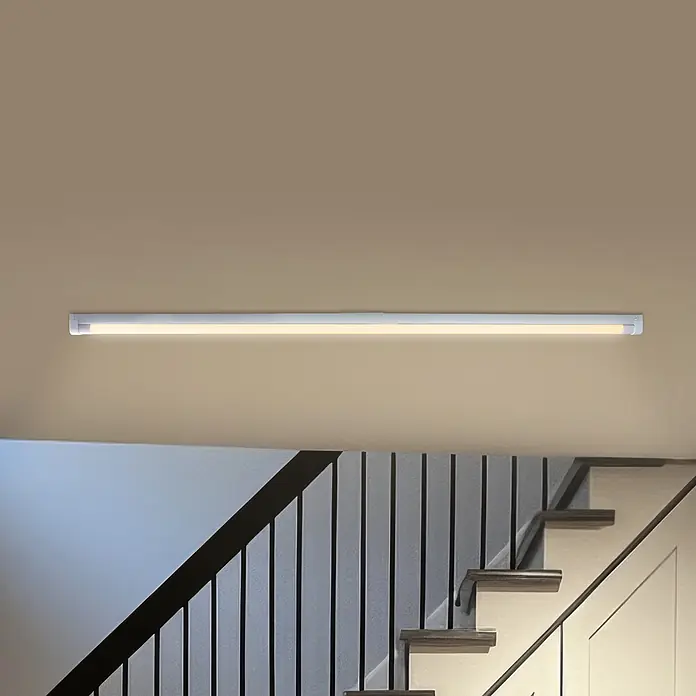 REV LED-Lichtleiste - L x B x H: 122,5 x 3,2 x 5,4 cm, Lichtfarbe: Neutralweiß, 18 W, 230 V - Weiße lineare LED-Leuchte an beigefarbener Wand, beleuchtet eine moderne Treppe.