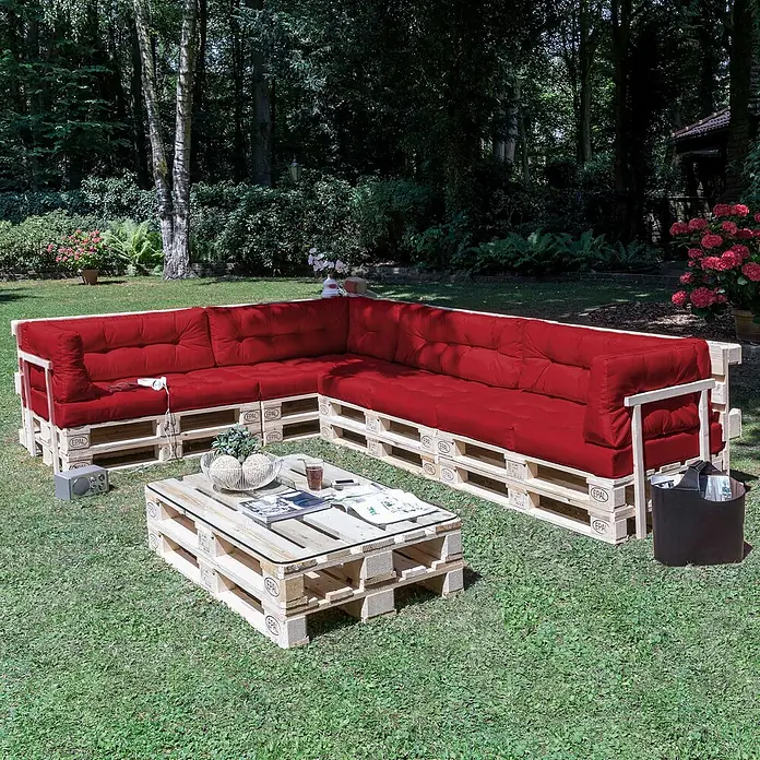 Beautissu Sitzauflage ECO Elements - Europalette, 1 Stk., L x B x H: 120 x 40 x 10 cm, Polyester, Rot - Outdoor-Ecksofa und Couchtisch aus hellen Holzpaletten mit leuchtend roten Kissen und Glasplatte, in einem Garten.