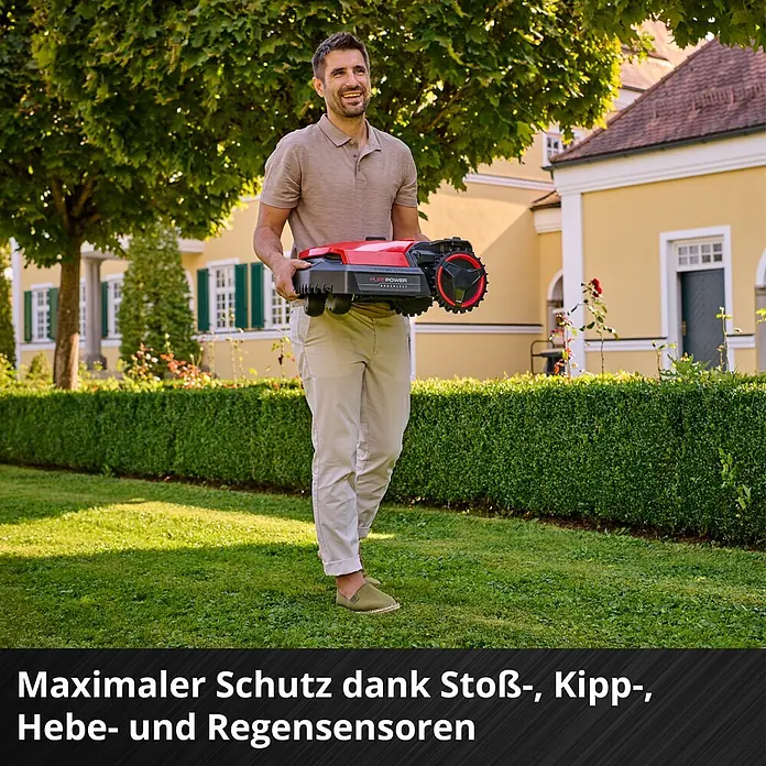 Einhell Power X-Change 18V Mähroboter Freelexo 500 - 500 m², Schnittbreite: 18 cm, Induktionsgestützte Navigation, Begrenzungskabel - Mann trägt einen roten und schwarzen Mähroboter in einem Garten.