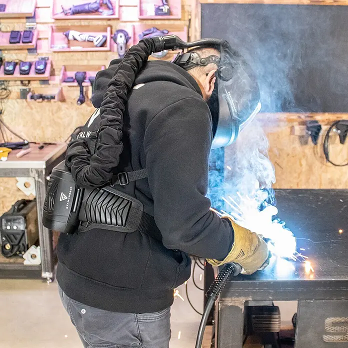 STAHLWERK Schweißhelm BOOSTER AIR Automatik Schweißhelm - Schwarz - Schwarze PAPR-Einheit am Rücken eines Schweißers, mit Schweißhelm verbunden, während des aktiven Schweißens im Einsatz.