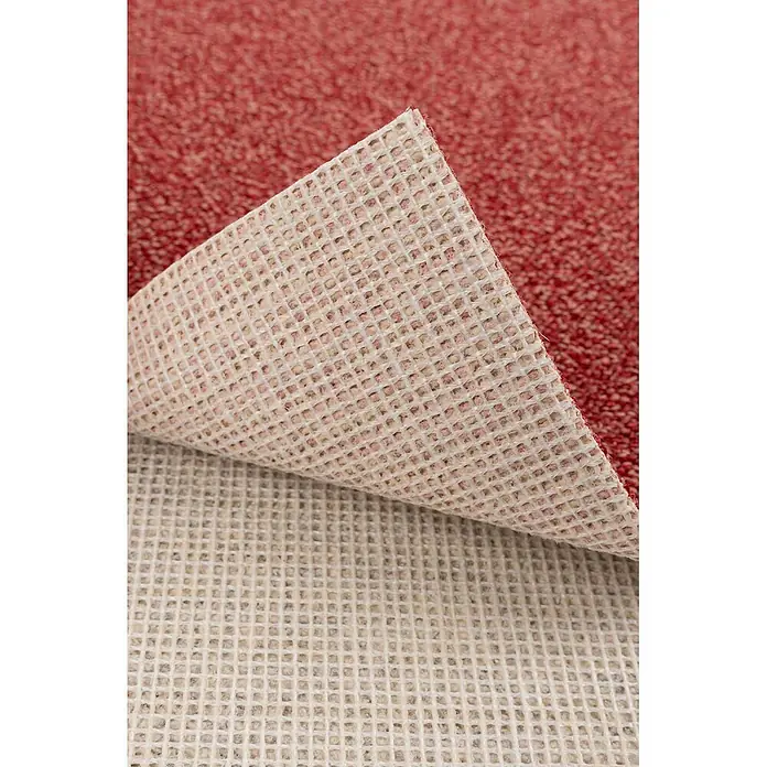 Bricoflor Teppichboden Meterware 5x4m, Schlinge meliert, rot - Schlinge, 100 % Polyamid (PA), rot - Roter Teppich mit angehobener Ecke, die seine helle, gittergemusterte rutschfeste Unterseite auf einer Antirutschmatte zeigt.