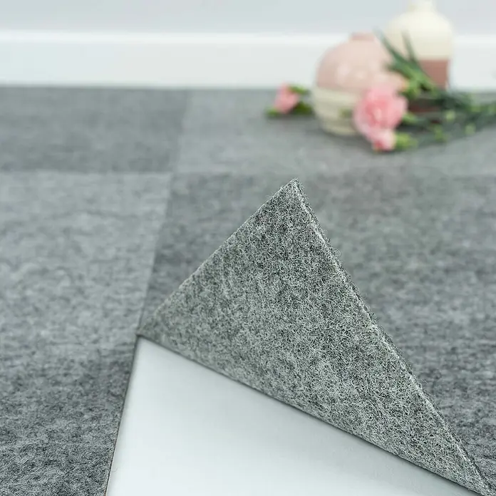 Teppichfliesen 40x40 cm selbstklebend Teppichboden Nadelvlies Grau -  - Selbstklebende graue Filzteppichfliese wird abgezogen, Klebefläche sichtbar.