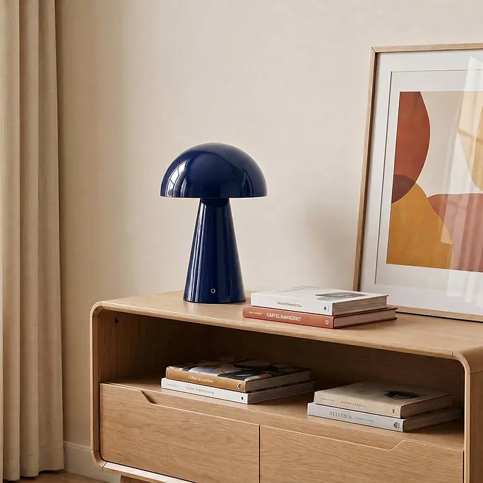 Lindby Tischleuchte Nevijo - blau, blau - Dunkelblaue, pilzförmige Tischlampe mit glänzender Oberfläche auf einem hellen Holzschrank zwischen Büchern.