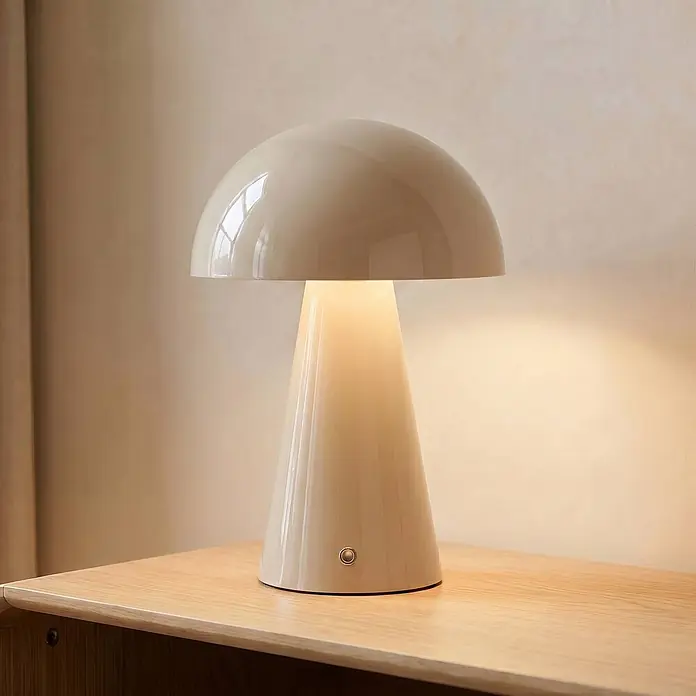 Lindby Tischleuchte Nevijo - creme / amber, creme / amber - Glänzende, cremefarbene Pilz-Tischlampe mit konischem Fuß, die warm auf einer Holzoberfläche leuchtet.