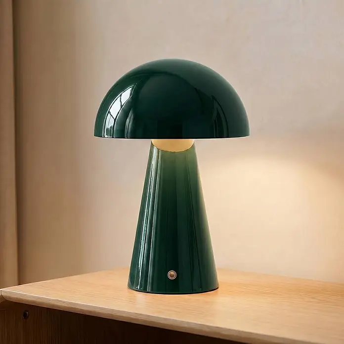 Lindby Tischleuchte Nevijo - grün, grün - Dunkelgrüne glänzende Pilz-Tischlampe mit geripptem Fuß und goldenem Akzent, beleuchtet auf einer Holzoberfläche.