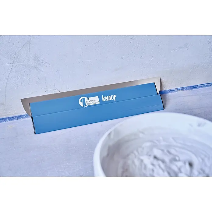 Knauf Glätt- & Flächenspachtel - 600 mm, Edelstahl - Blauer Knauf Spachtel mit Metallklinge, bereit zum Verputzen neben einem Eimer Spachtelmasse.