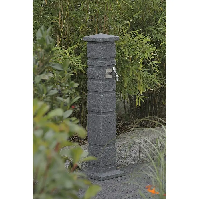 Arves Wasserzapfstelle Romana - Black Granitfarben, Höhe: 110 cm, Ausstattung: Wasserhahn - Moderner Steingartenbrunnen mit Wasserhahn. Der Brunnen ist aus grauem Stein gefertigt und steht inmitten üppiger Vegetation.