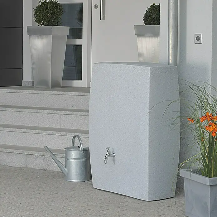 Arves Regenspeicher Noblesse - 275 l, Granitfarben, 1 Stk. - Regenwasserbehälter im Garten neben einer Gießkanne. Ideal für die umweltfreundliche Gartenbewässerung.