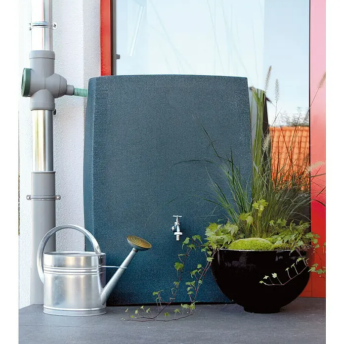 Arves Regenspeicher Noblesse - 275 l, Black Granitfarben, 1 Stk. - Nahaufnahme einer Regentonne mit Wasserhahn, neben einer silbernen Gießkanne und einem großen Pflanzgefäß.