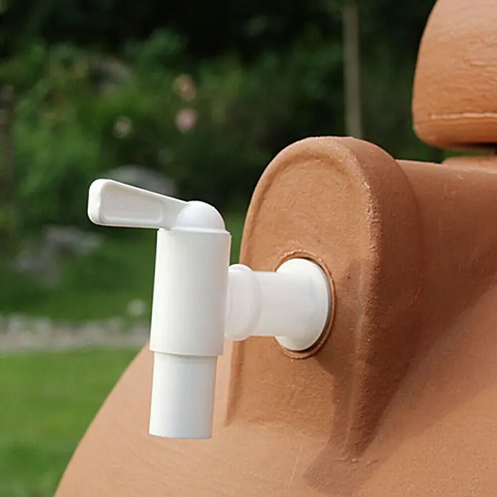 Arves Auslaufhahn aus Kunststoff - Gewindegröße Wasserhahn: ¾″, Zubehör: Bohrer - Nahaufnahme eines Wasserhahn aus Kunststoff, montiert an einem Terrakotta-Gefäß. Fokus liegt auf dem Zapfhahn und seiner Befestigung.
