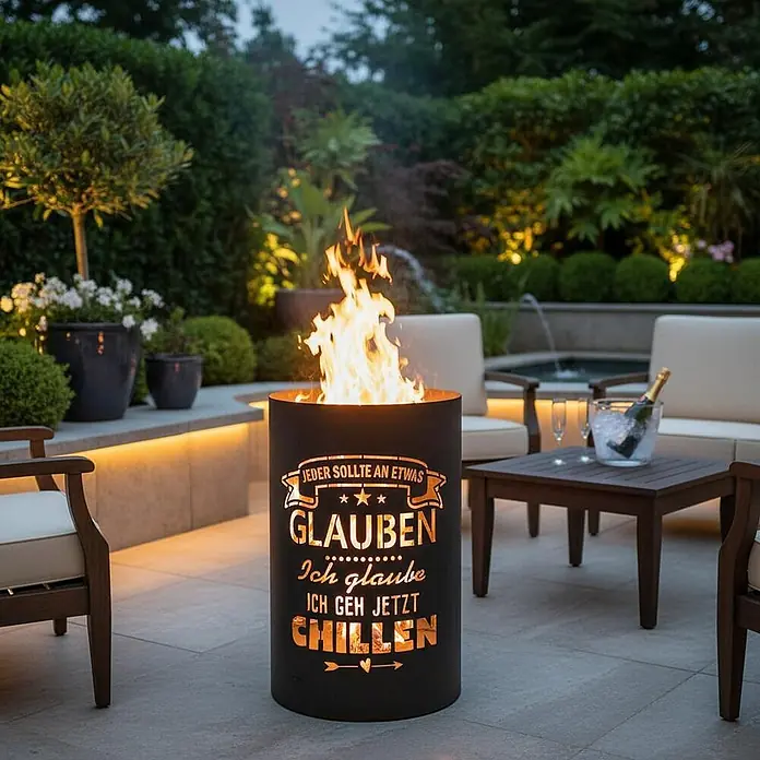 TiKo-Design® Feuertonne Chillen Ø 40 cm – massive Feuerstelle -  - Schwarze Metall-Feuerschale mit ausgeschnittenem deutschen Text über Glauben und Chillen, leuchtet mit Feuer im Garten.