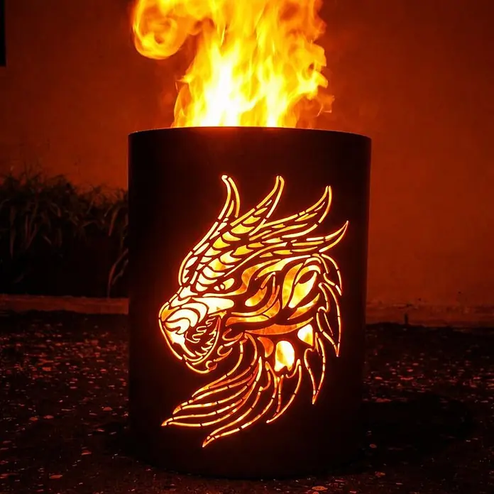TiKo-Design Holzkohlegrill Feuertonne-Drachen - grau - Dunkle Metall-Feuerschale mit leuchtendem Drachen-Ausschnitt, brennt aktiv mit hellen orangefarbenen Flammen.