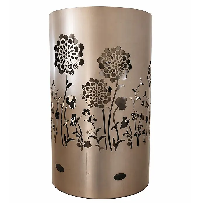 TiKo-Design Holzkohlegrill Feuertonne-Flower Power - grau - Zylindrischer Behälter aus gebürstetem Metall in Hellbronze mit filigranen Blumenmotiven, die eine Gartenlandschaft bilden.