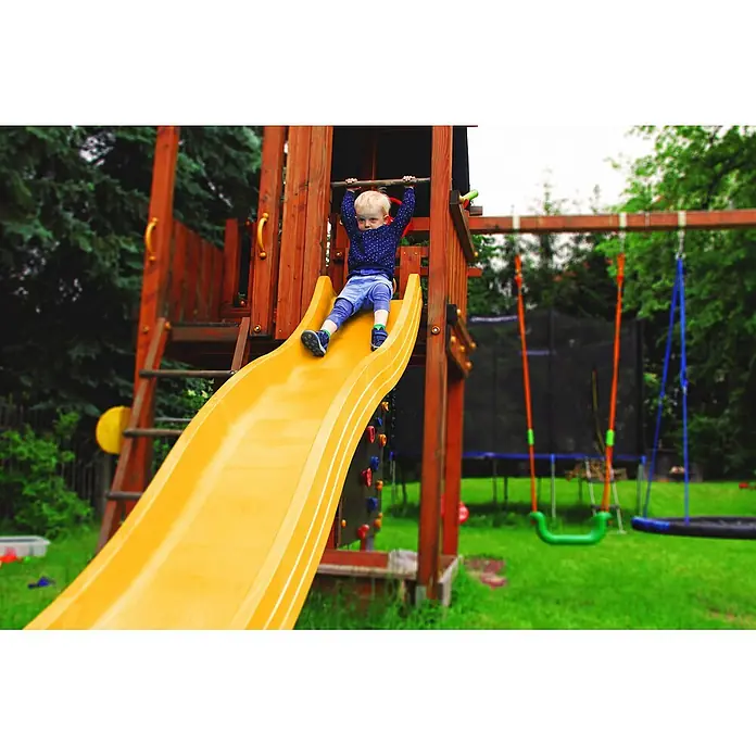 Wellenrutsche Anbaurutsche 3,00 x 0,50 m gelb -  - Ein kleines Kind sitzt auf einer gelben Spielplatzrutsche und hält sich an einer Stange fest, auf einem Holzspielplatz.
