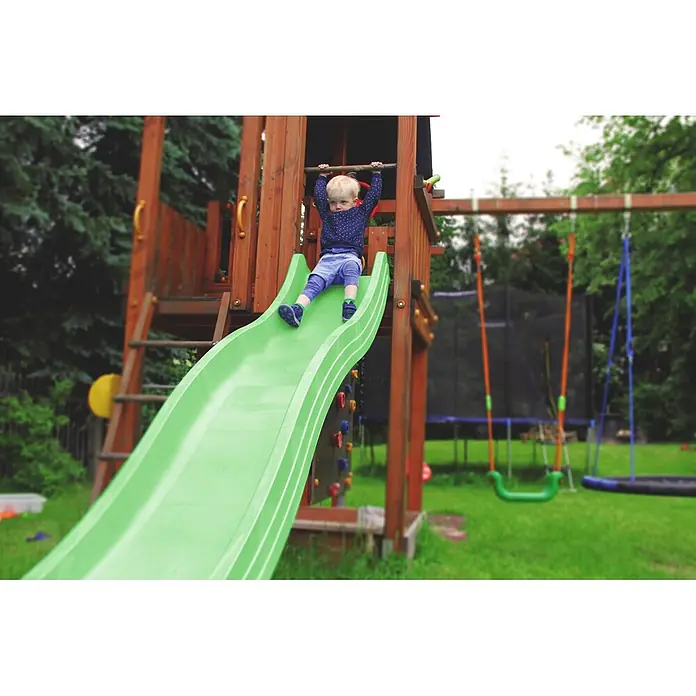 Wellenrutsche Anbaurutsche 3,00 x 0,50 m Apfelgrün -  - Ein kleines Kind sitzt oben auf einer grünen Rutsche an einem Holzspielplatz und ist bereit zum Rutschen.