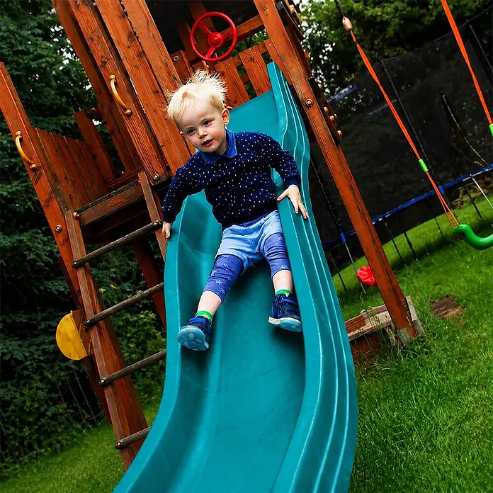 Wellenrutsche Anbaurutsche 3,00 x 0,50 m Türkis -  - Ein kleiner Junge rutscht eine grüne Spielplatzrutsche hinunter, Teil eines Holzspielturms.