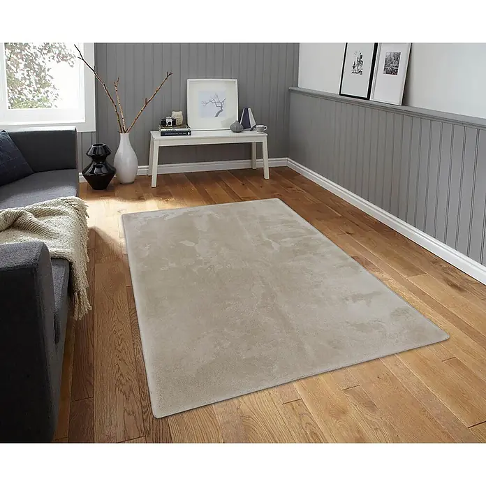 Alfombra de pelo largo Cuba - Camel, 170 x 120 cm, 100% Poliéster - Alfombra rectangular beige de textura suave sobre suelo de madera, parcialmente bajo un sofá gris oscuro en una sala.
