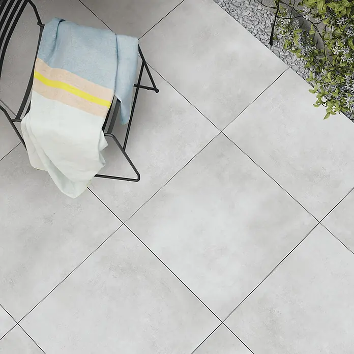 Terrassenfliese Dimension - 59,8 x 59,8 x 2 cm, Grau, Matt - Hellgraue Outdoor-Terrassenfliesen mit dunkler Fuge, diagonal verlegt, neben Pflanze und Wäscheständer.