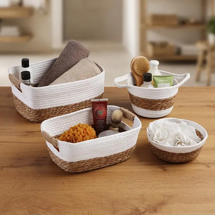 Versa Cesta - L x An x Al: 31 x 23 x 13 cm, Blanco, Fibra natural - Juego de cestas tejidas blancas y marrones con toallas, esponjas y artículos de tocador sobre una superficie de madera.